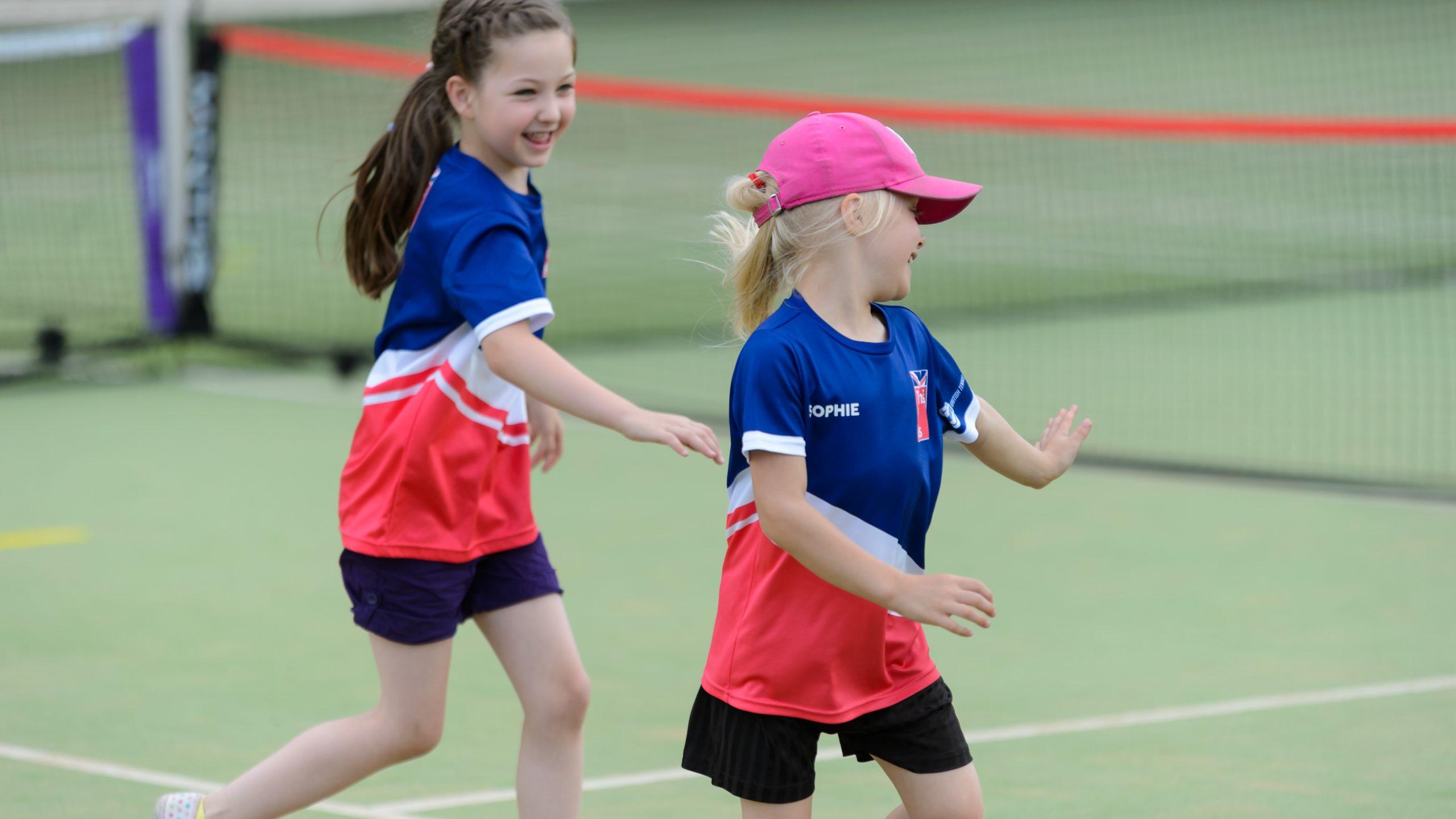 Two primary school girls running on a tennis court