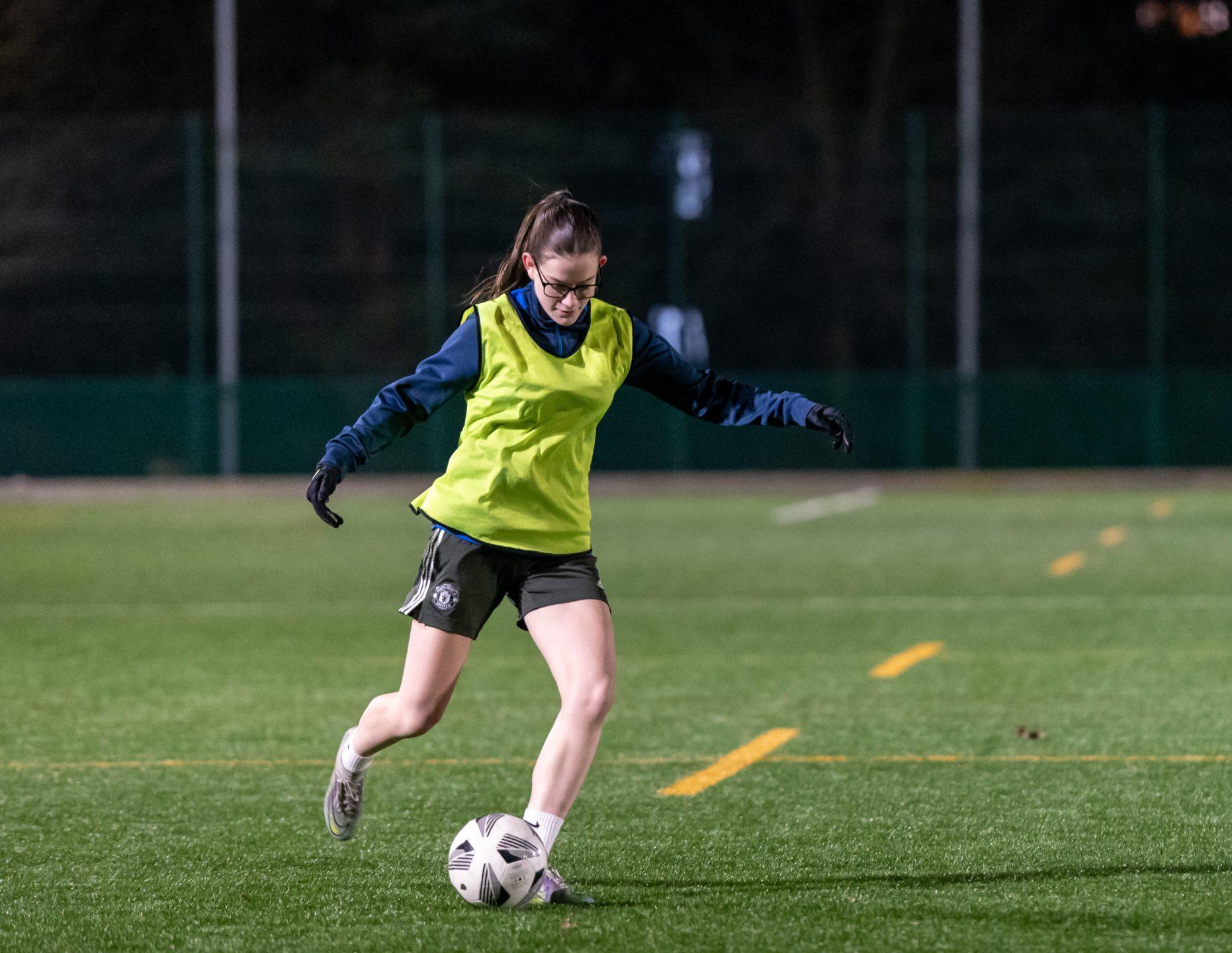 Young white woman aged 20-30 kicking a football