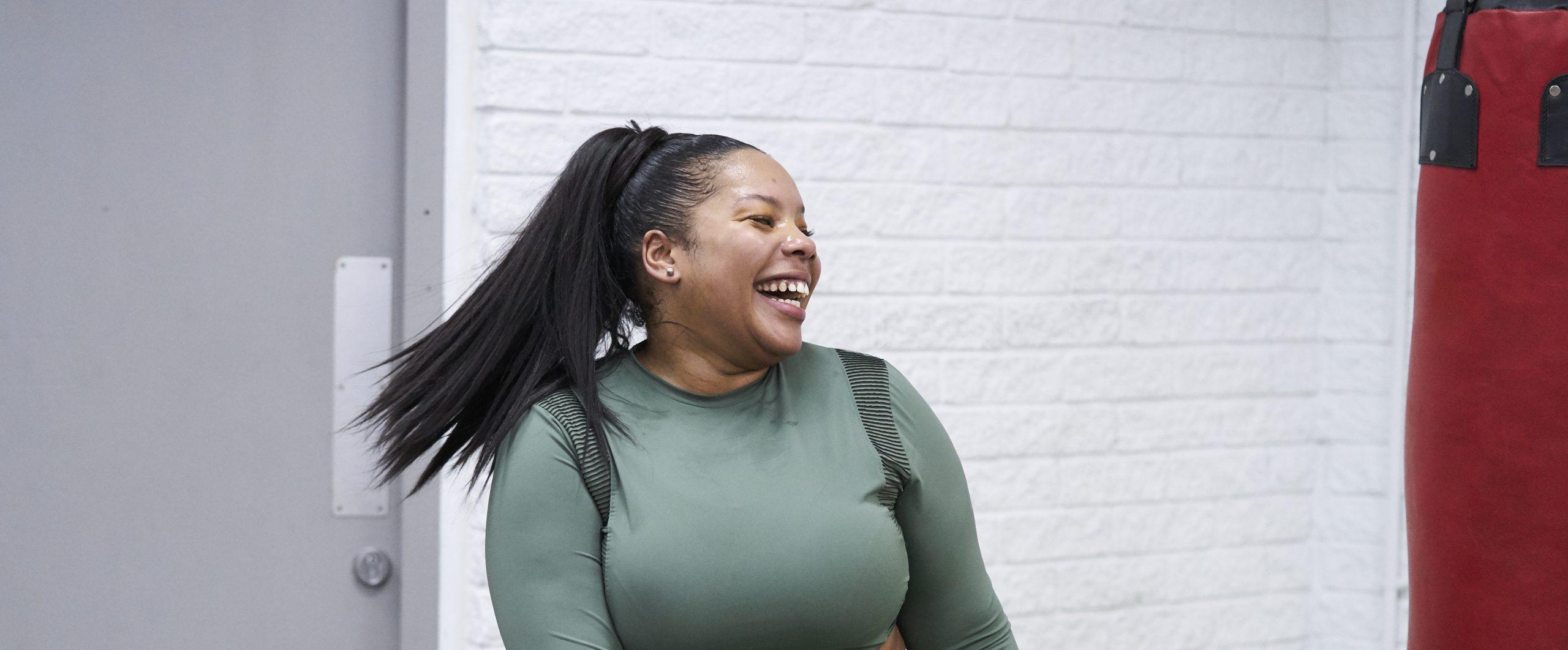 A black woman aged 25-30 laughing while practicing boxing