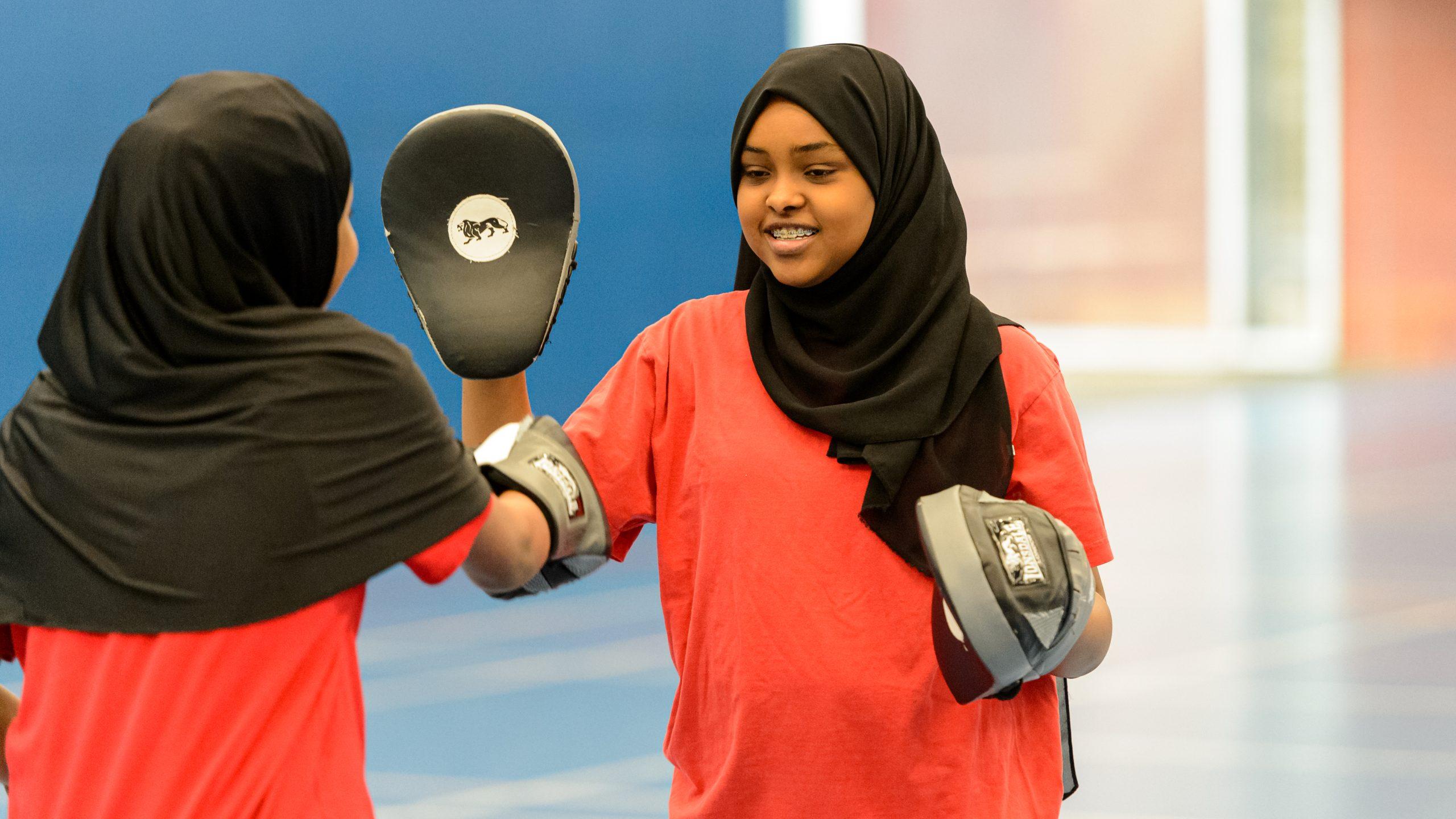 Two teenage girls wearing headscarves boxing