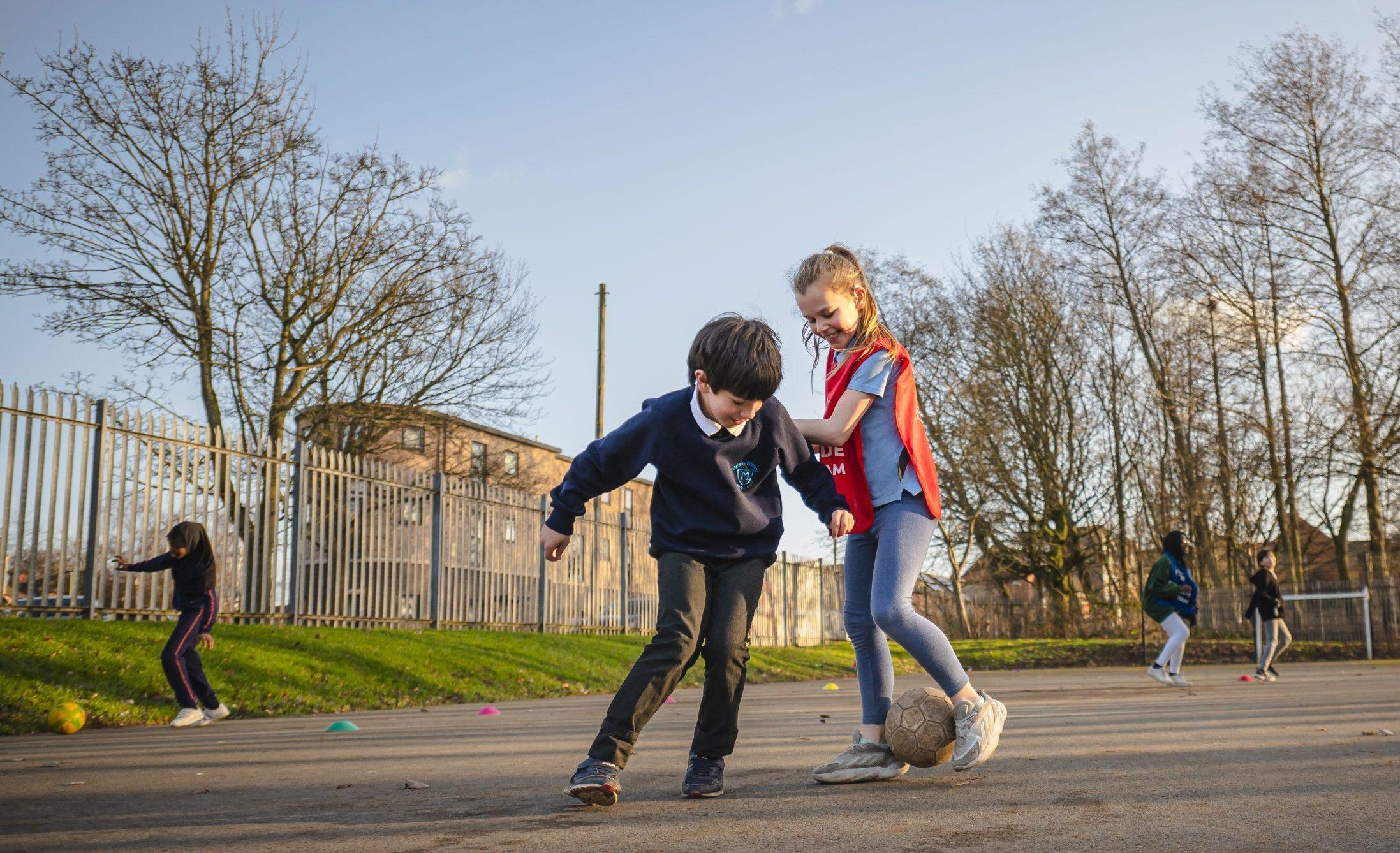 A young boy and girl playing football together at school