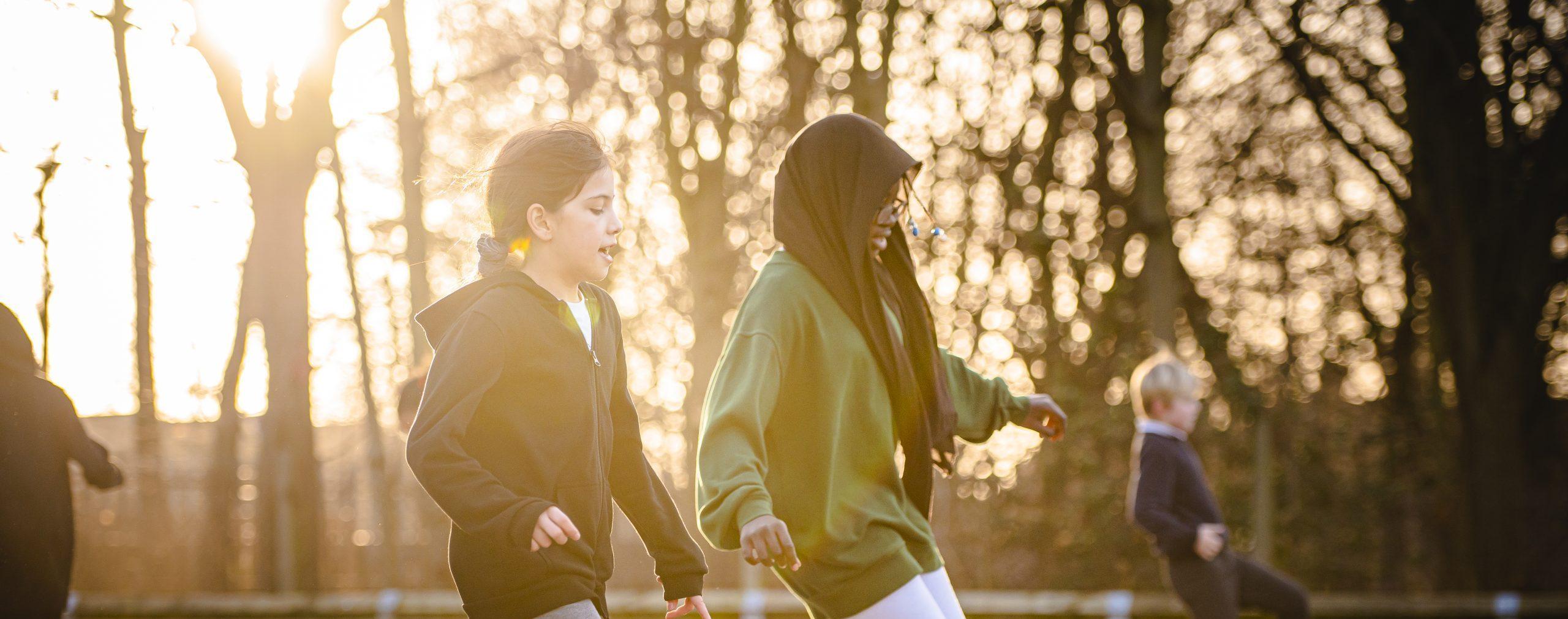 Two young girls playing football at school, one is white with brown hair, the other is black and wearing a head scarf