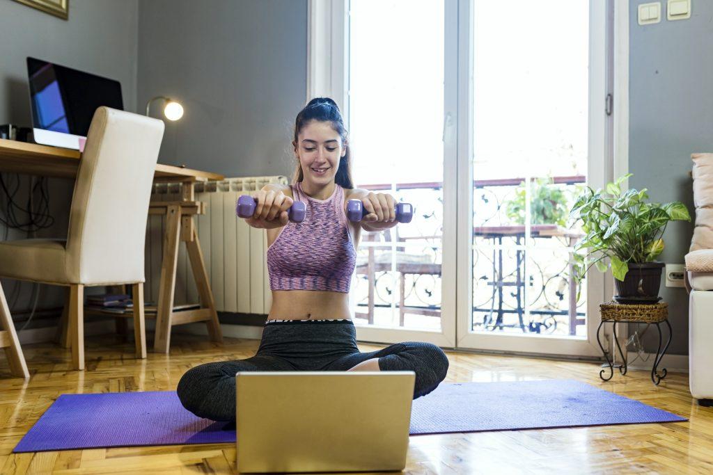 Teenage girl exercising at home.She is using a laptop and smartphone to communicate with friends on social media.