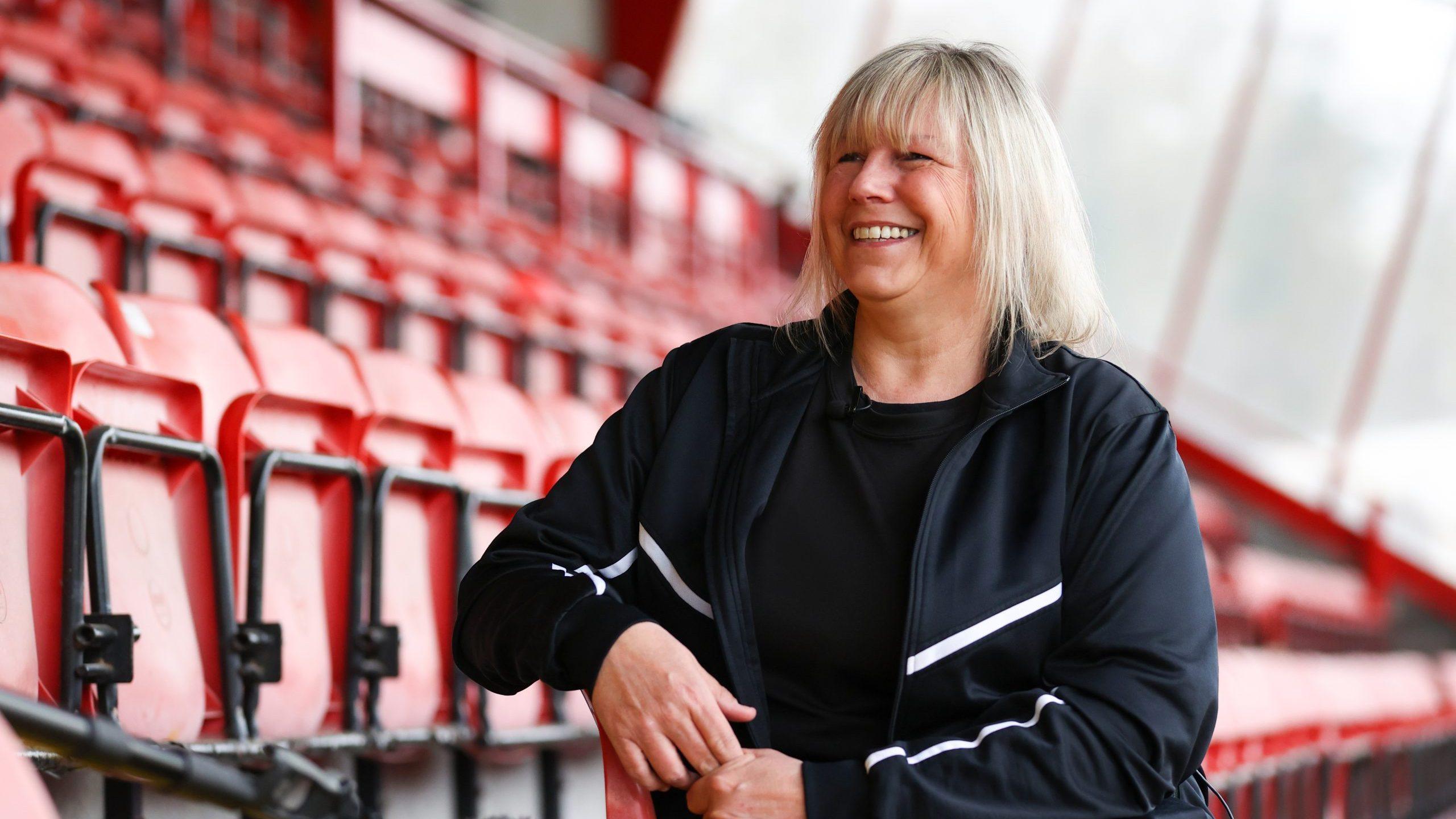 A white woman aged 50-55 sat in football stands smiling