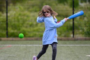 A young girl hitting a ball with a rounders bat