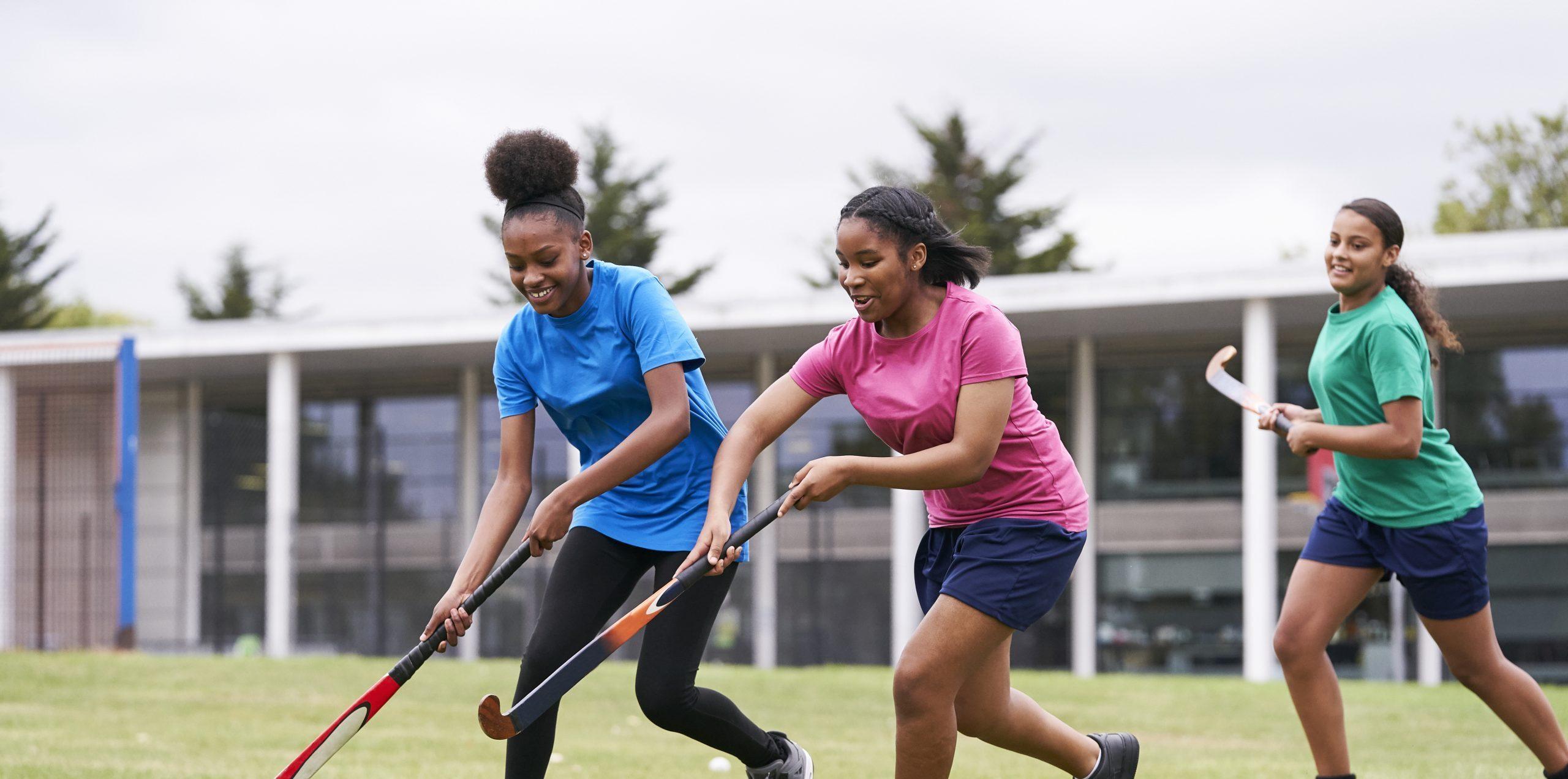 Two black teenage school girls playing hockey on grass